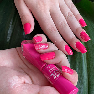 Manicure rosa com acabamento brilhante ao lado de frasco de esmalte